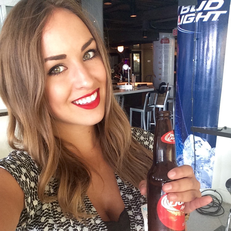 Woman holding a beer bottle in an indoor setting with a Bud Light sign.