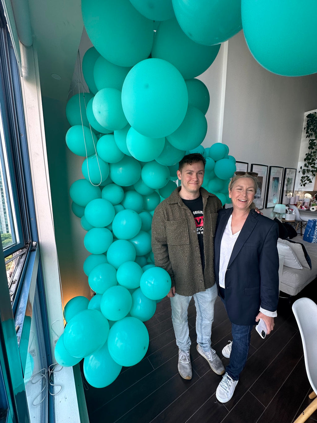 Two people standing in front of a teal balloon archway.