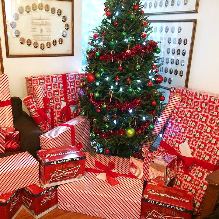 Christmas tree with red and green decorations surrounded by budweiser wrapped presents in a room.
