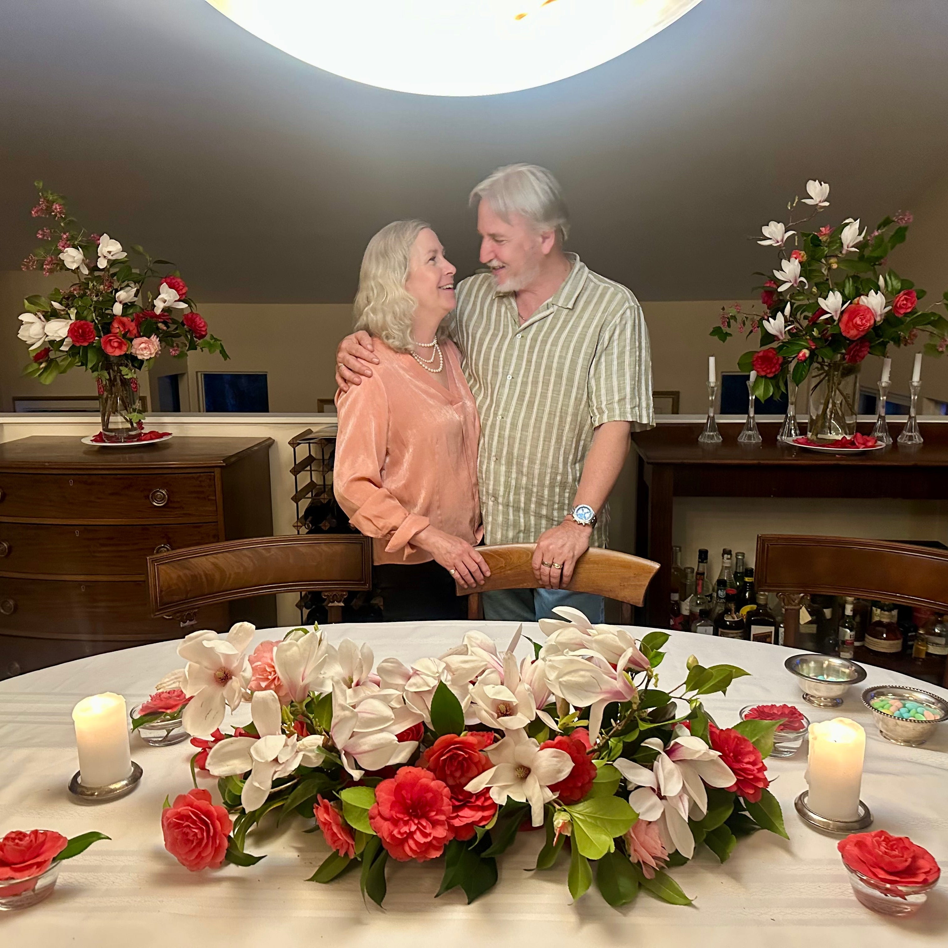 Couple embracing in a room with floral arrangements and candles on a table.