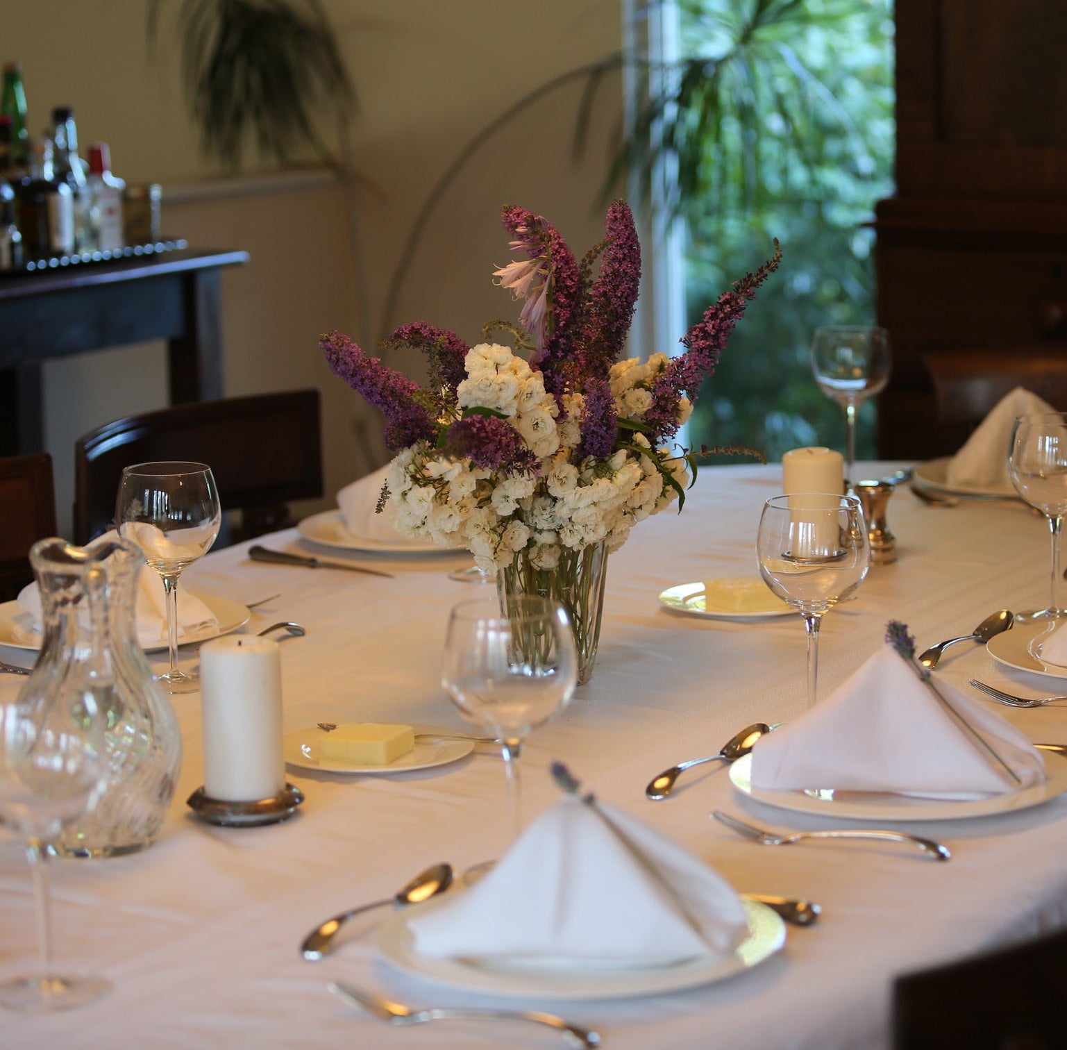 Dining table set with place settings, glasses, and a floral centerpiece.
