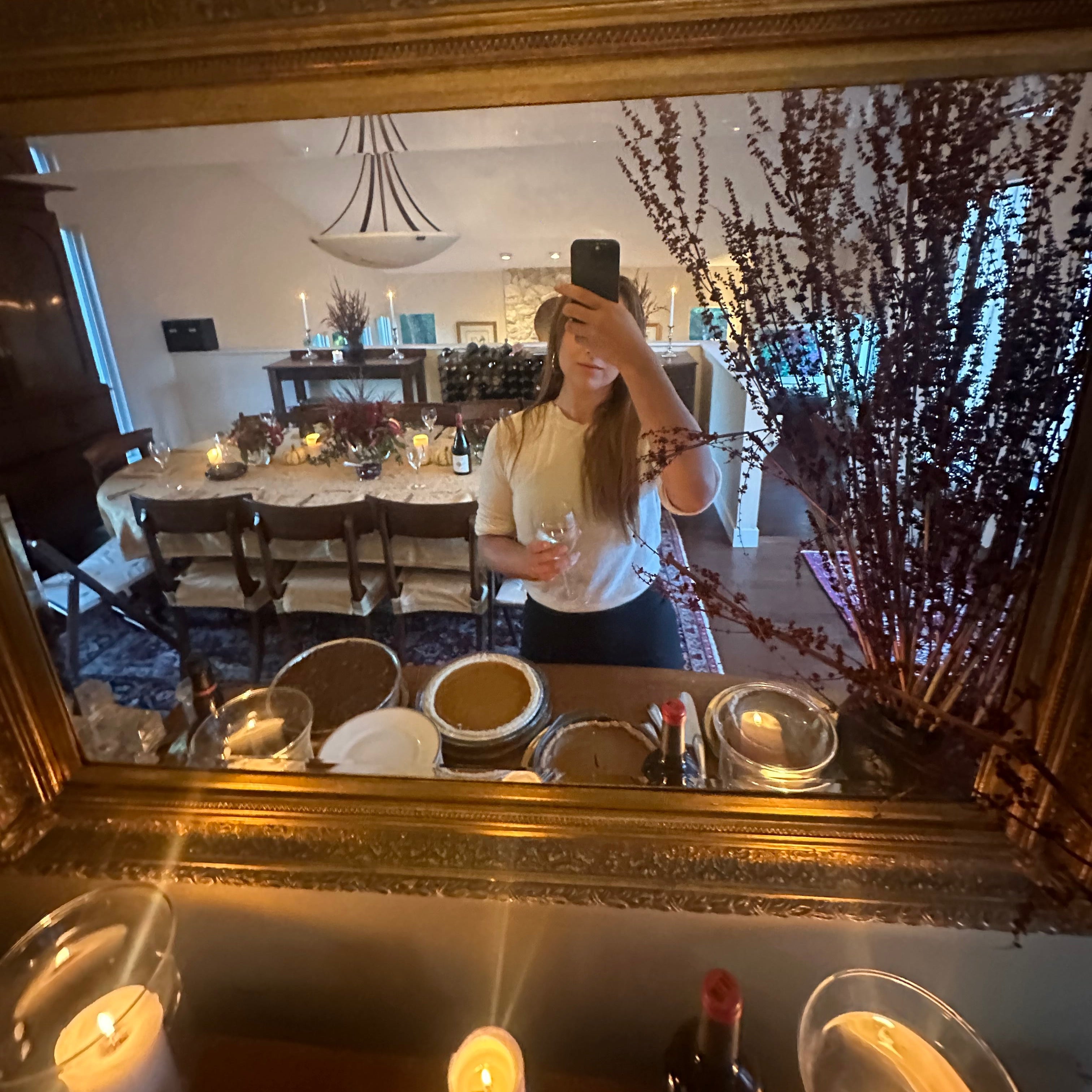 Decorative mirror with gold frame reflecting a room with candles and a bottle.