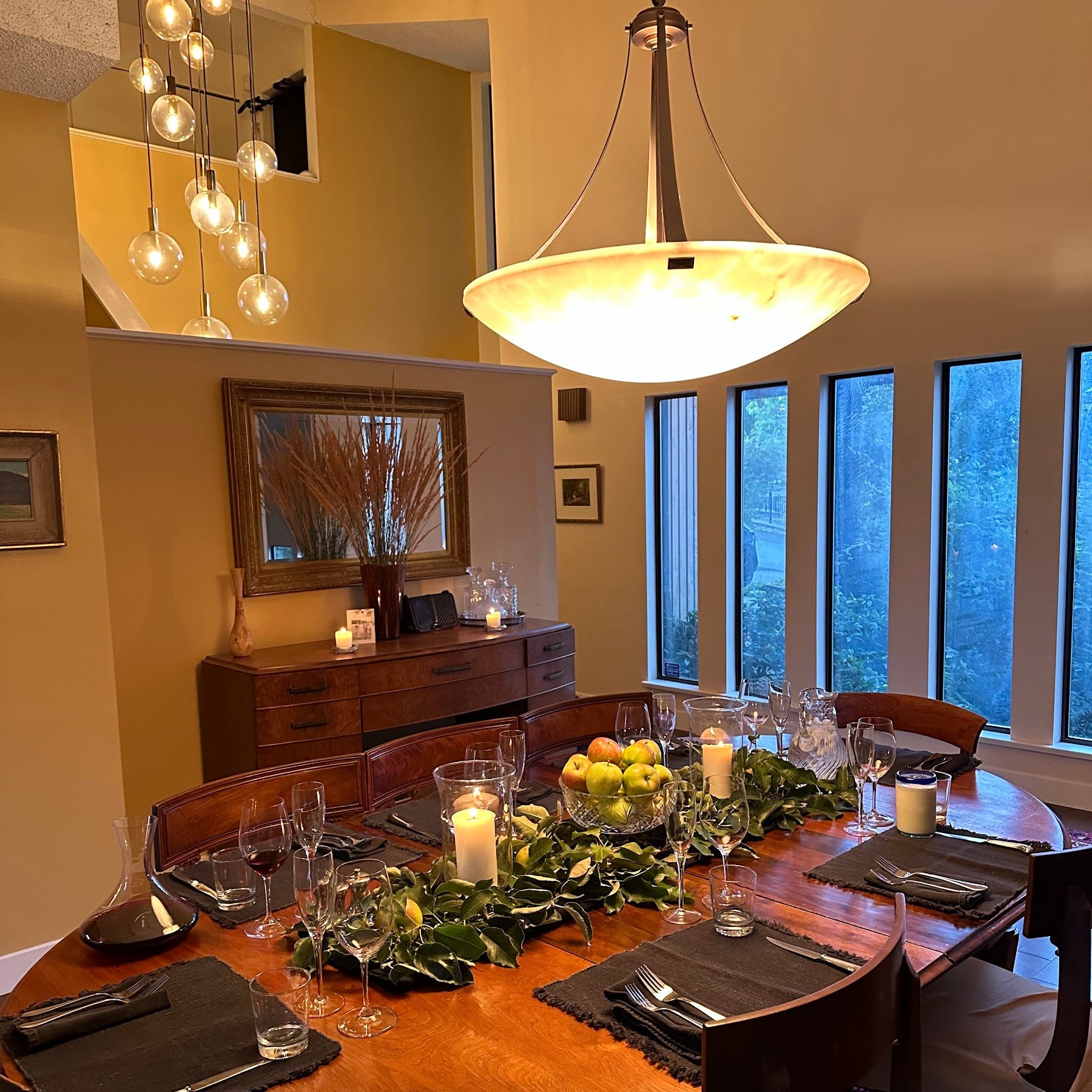 Dining room with a wooden table set for a meal, featuring candles and fruit.