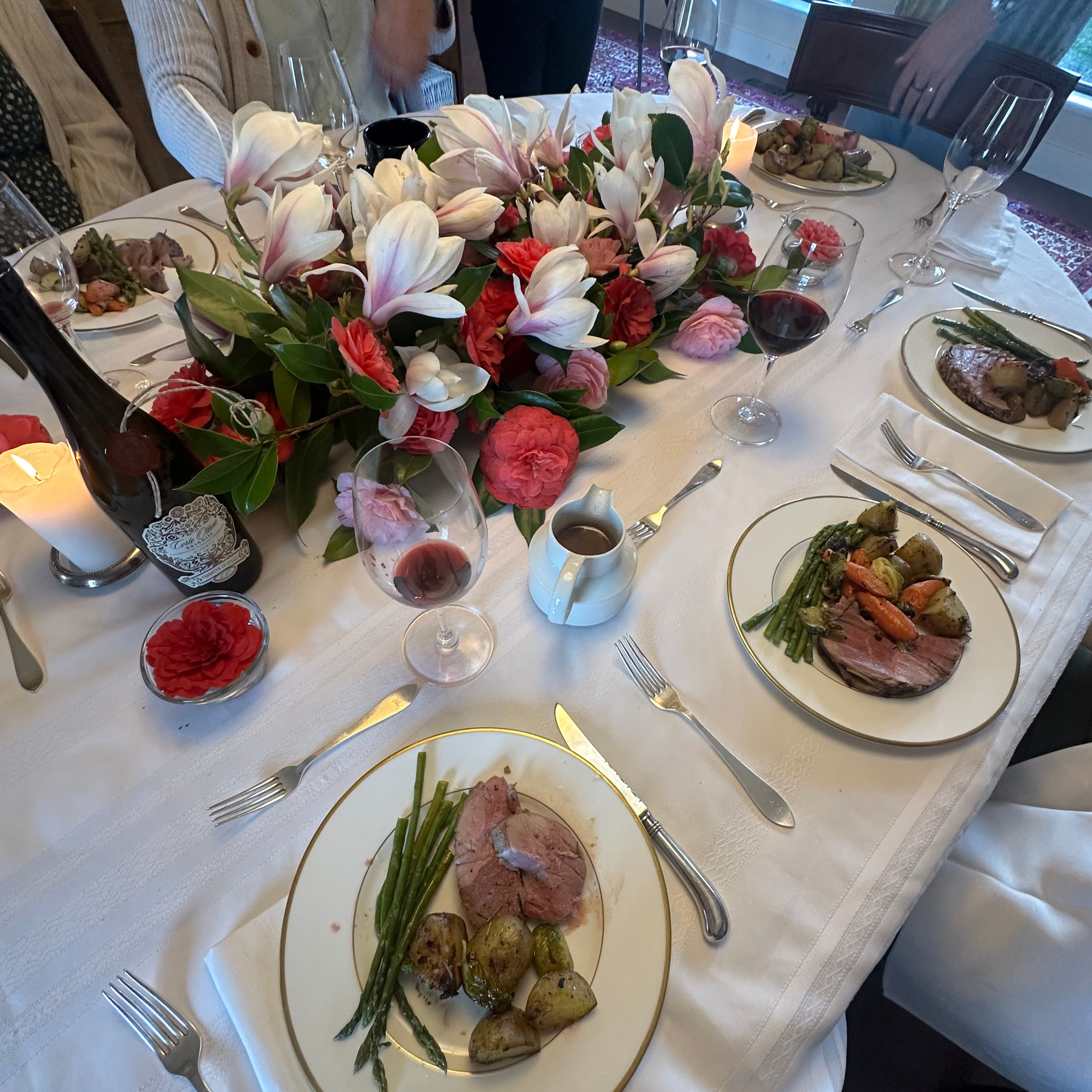 Dining table set with plates of food, flowers, and wine glasses.