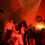 Group of people in a dimly lit room with red lighting, sitting around a table.