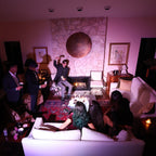 Group of people in a dimly lit room with a fireplace and decorative items.