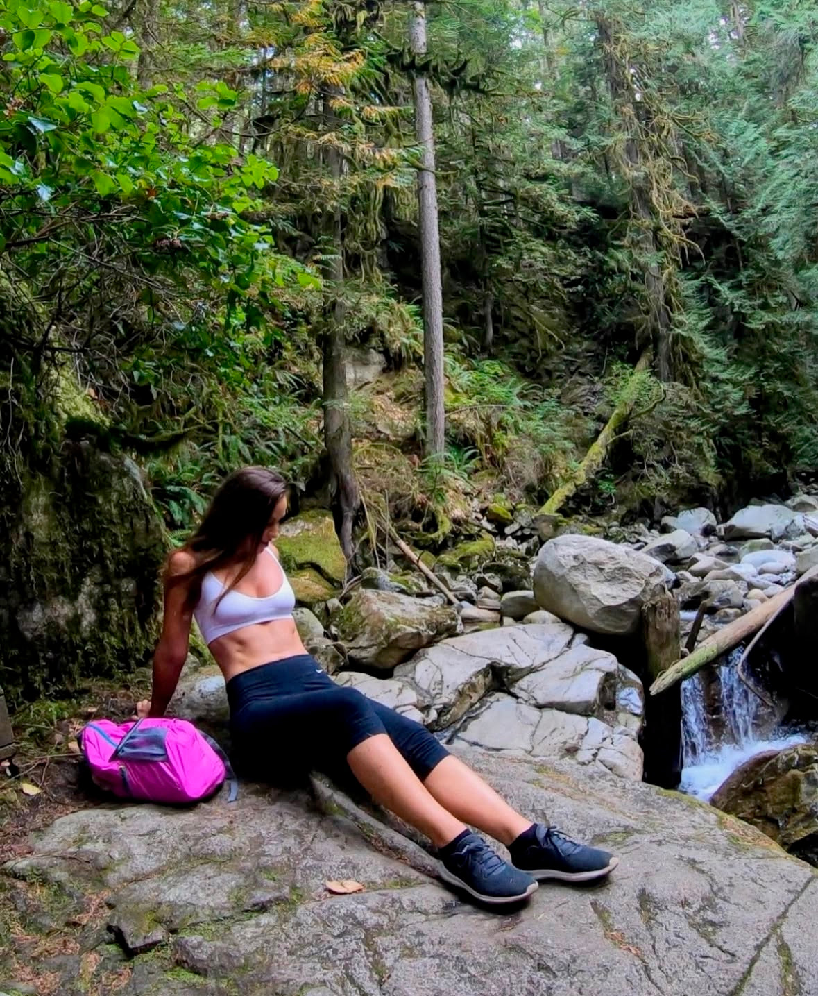 Person sitting on a rock in a forest with a pink backpack