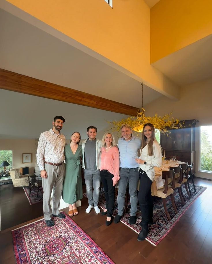 Group of six people posing in a modern living room with yellow walls and wooden floors.