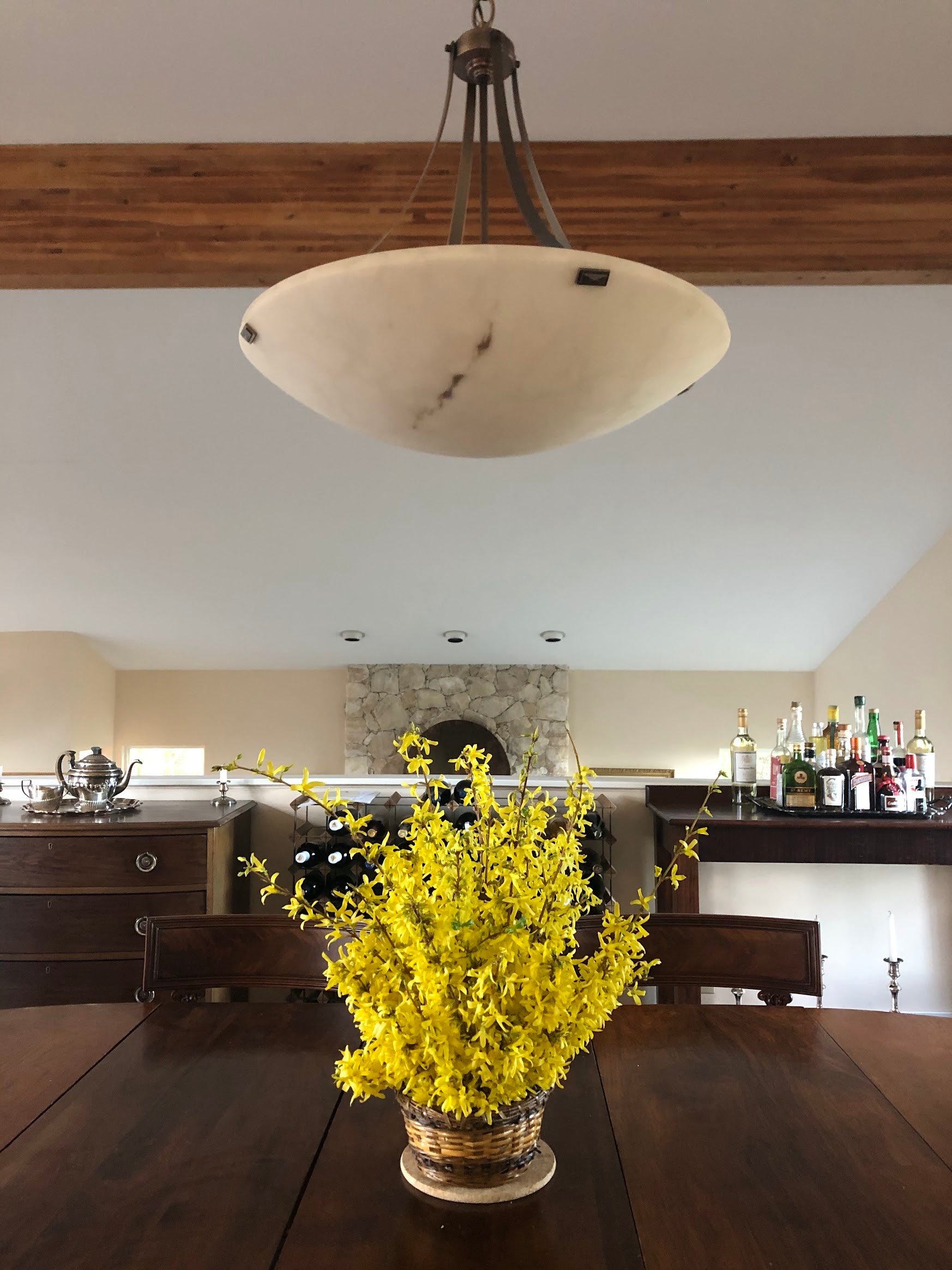 Dining room with a table, yellow flowers in a vase, and a hanging light fixture.