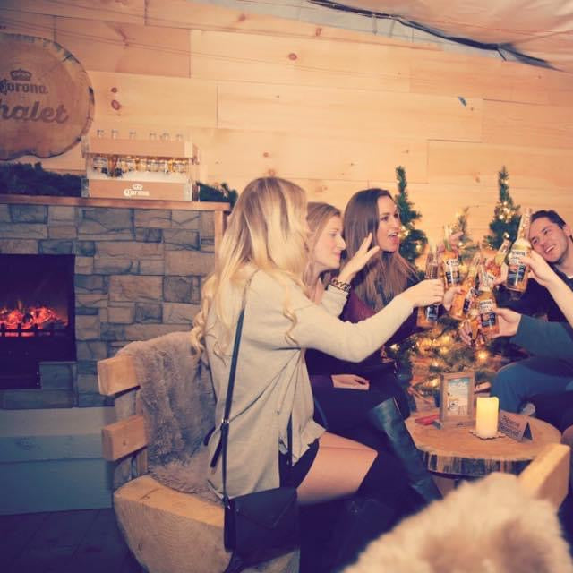 Group of people enjoying a festive gathering with drinks and a Christmas tree in a cozy indoor setting.