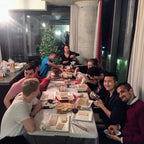 Group of people sitting around a table in a modern kitchen with a Christmas tree in the background.
