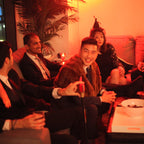 Group of people sitting on a couch in a dimly lit room with warm lighting.
