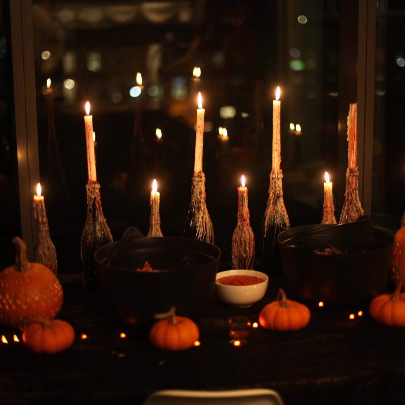 Halloween-themed table setting with candles and pumpkins in a dark room.