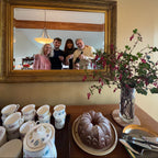 Gold-framed mirror reflecting a group of people in a room with decorative elements.