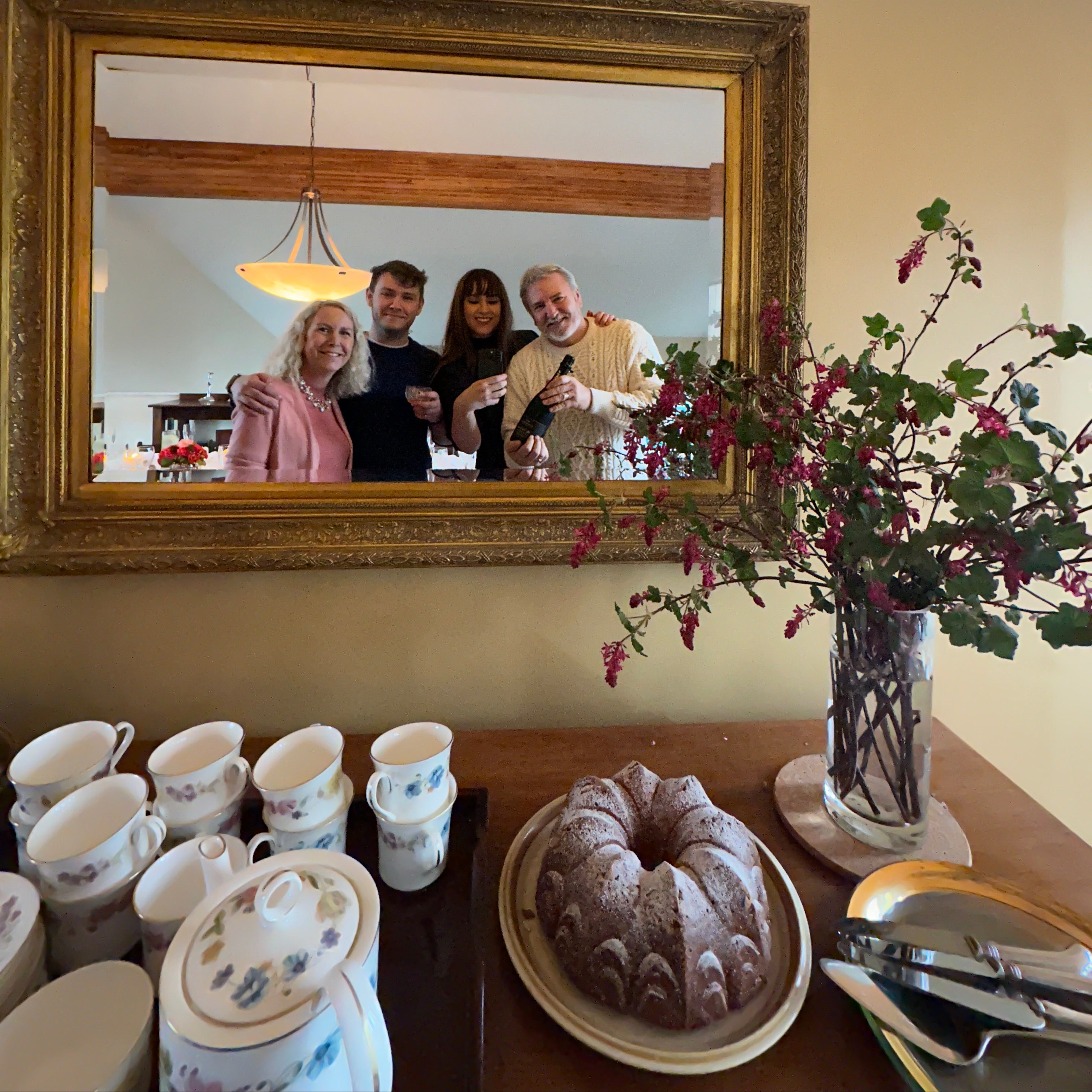 Gold-framed mirror reflecting a group of people in a room with decorative elements.