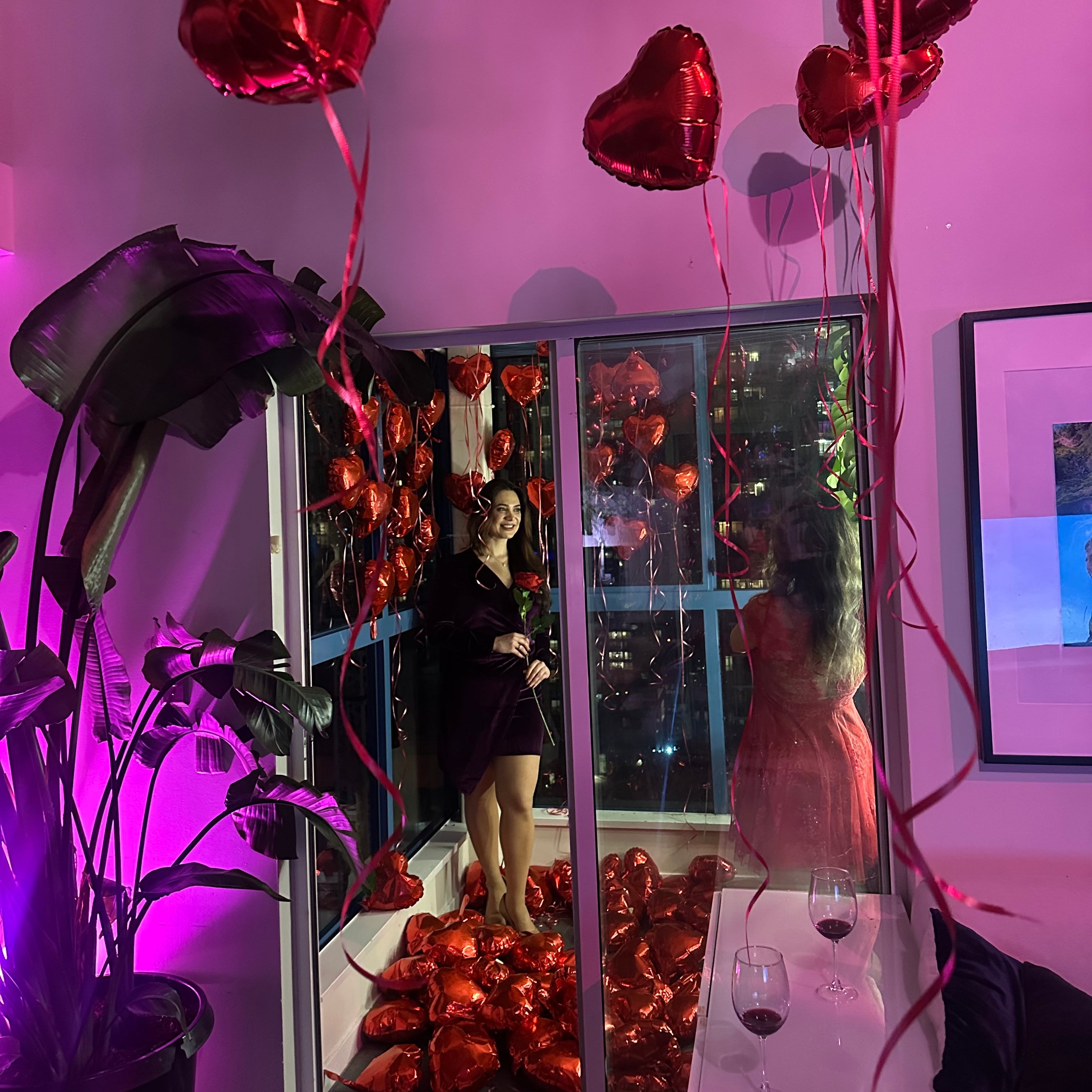 Laptop with a video playing on a reflective surface, surrounded by red heart-shaped balloons.