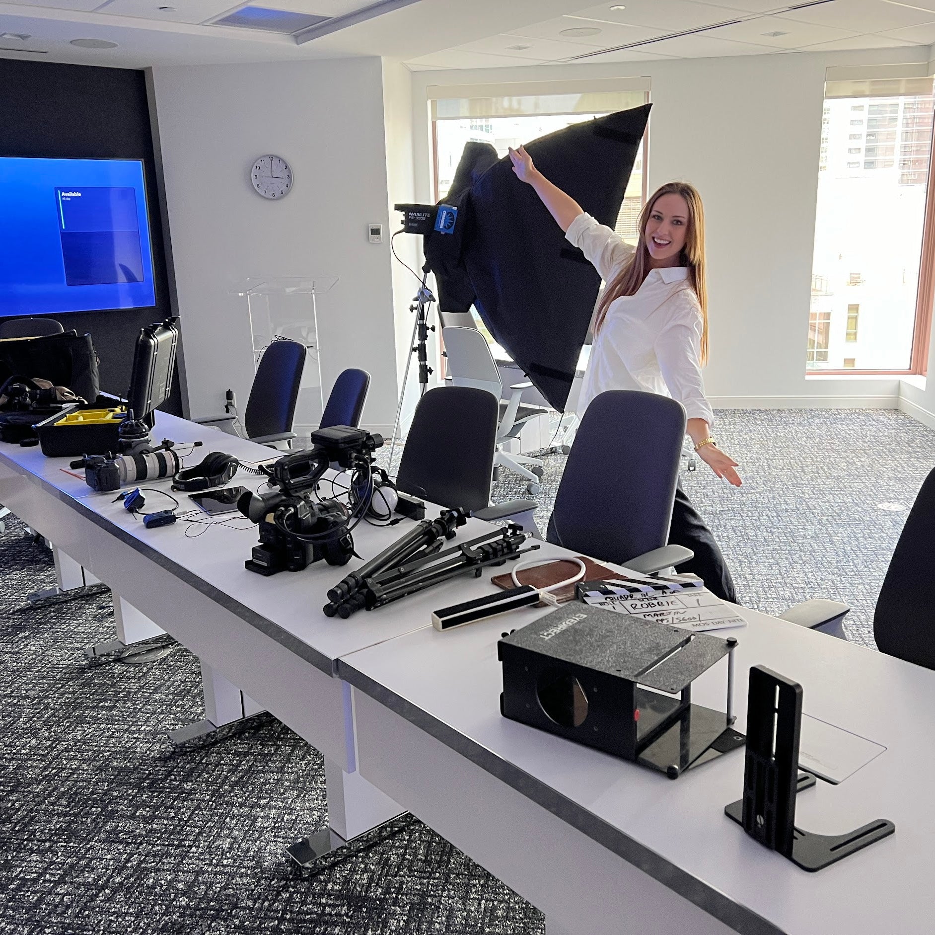 Person setting up camera equipment in a modern office with large windows.