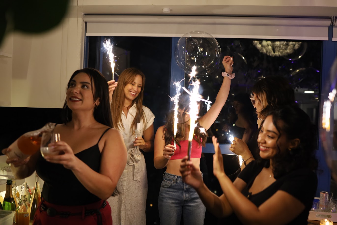 Group of women celebrating with sparklers indoors.