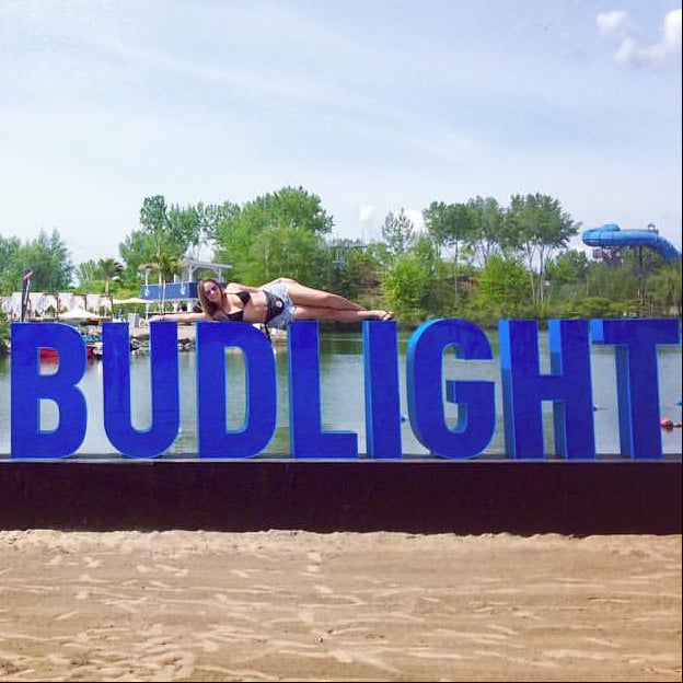 Large blue sign with 'LAVIEBUDLIGHT' on a beach with people and boats in the background.