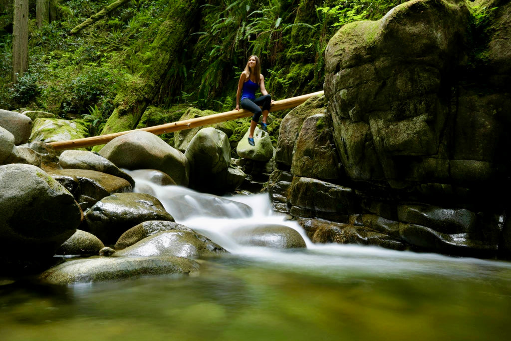 Person standing on a log over a stream in a forest