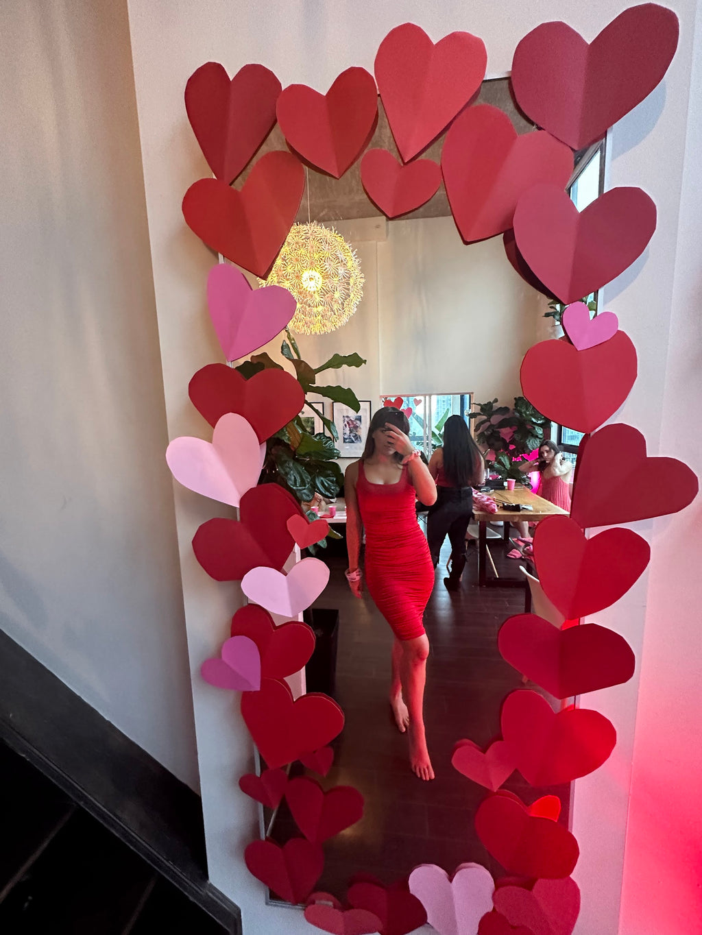 Woman in a red dress standing in front of a heart-shaped mirror frame.