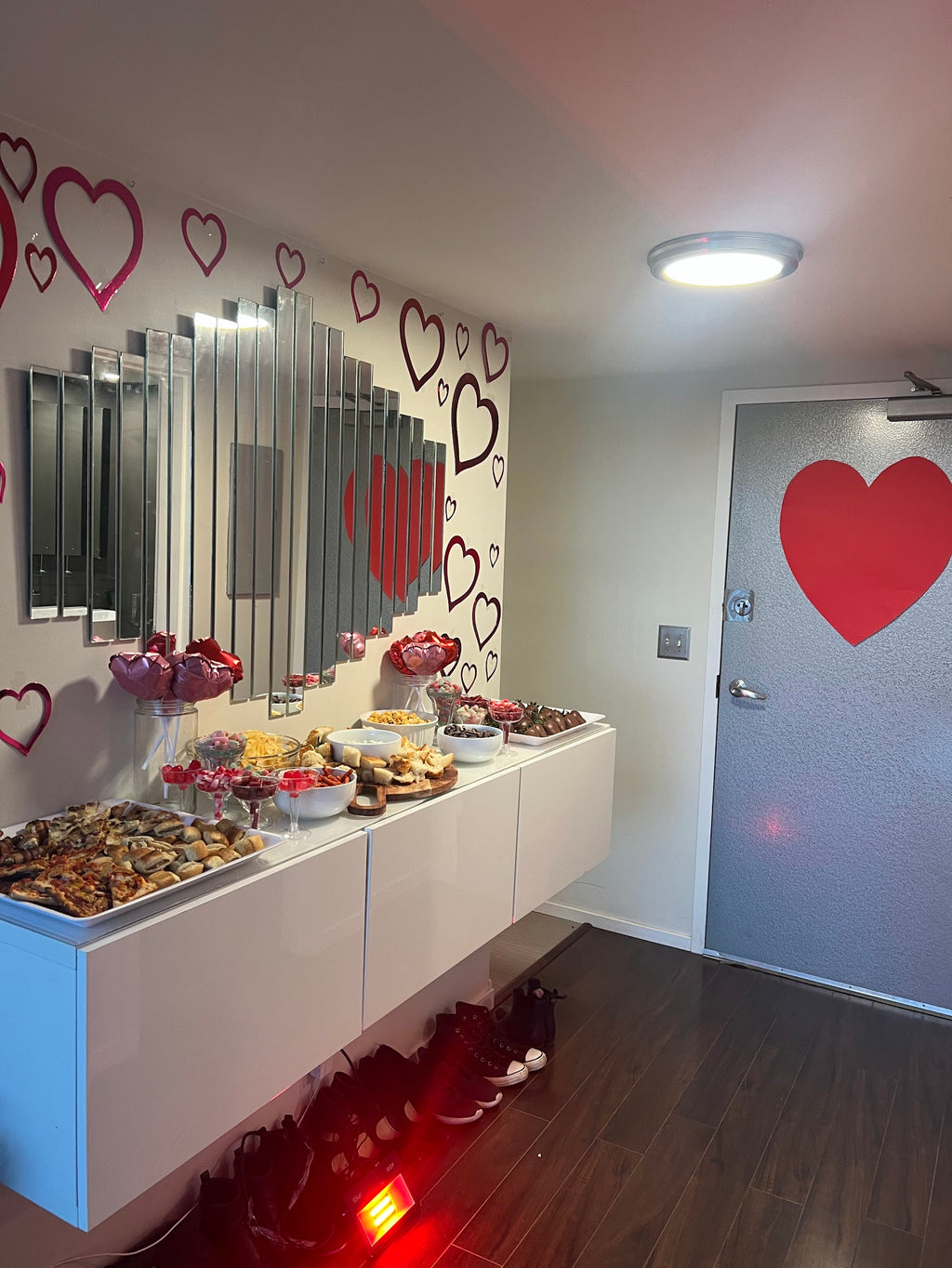 Dessert table with various treats in a room decorated with heart shapes on the wall and door.