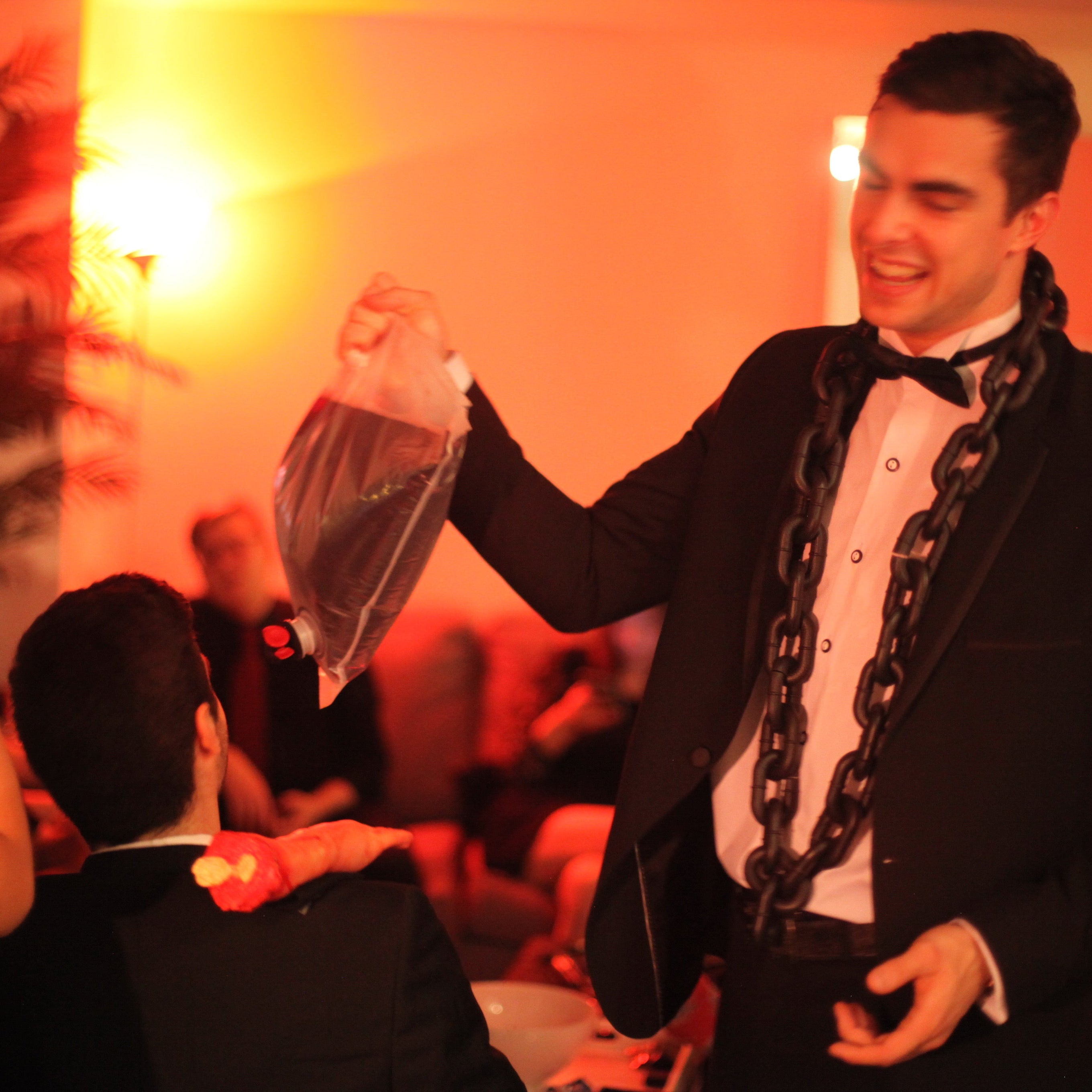 Man in a tuxedo with a chain around his neck at a party.
