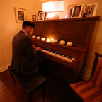 Man playing a piano in a dimly lit room with framed pictures on the wall.