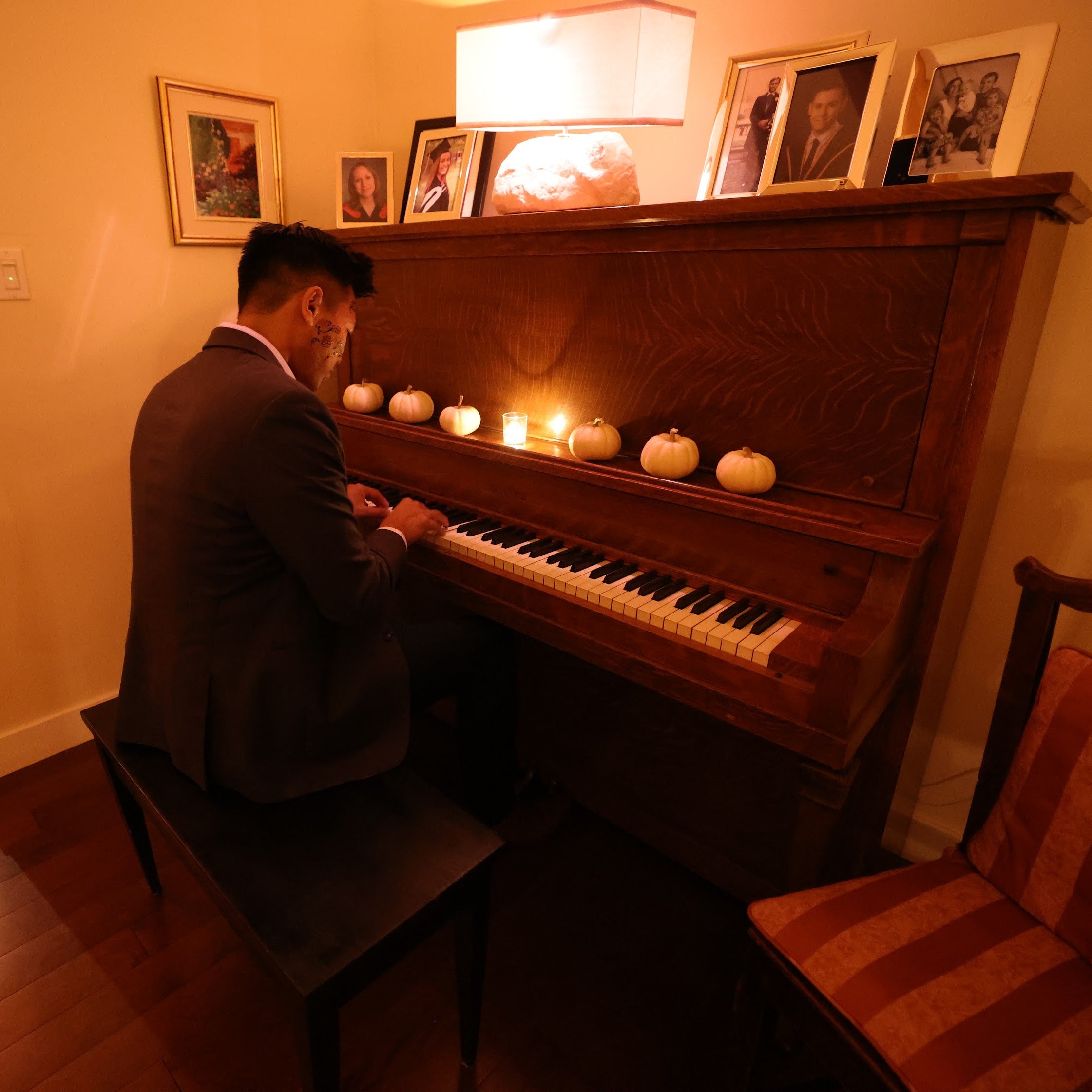 Man playing a piano in a dimly lit room with framed pictures on the wall.