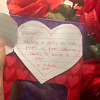 Notebook with handwritten message on a red heart-shaped box surrounded by red roses.
