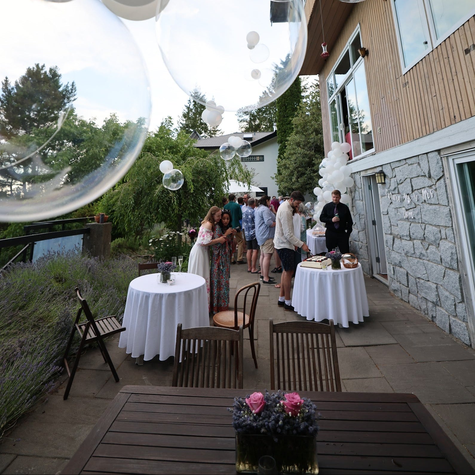 Outdoor event with tables, chairs, and people near a building with bubble decorations.