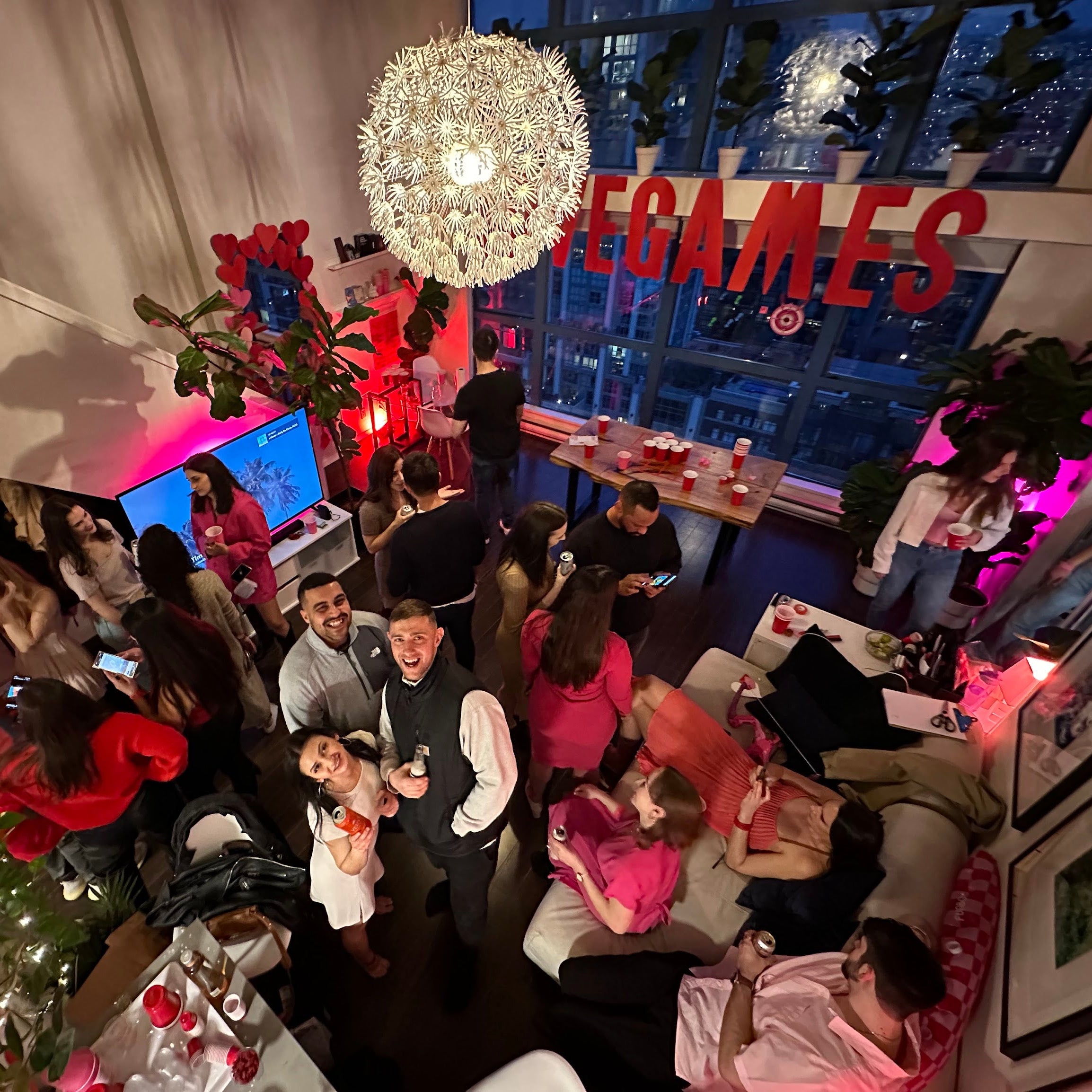 Party scene with people socializing, a chandelier, and a 'LOVEGAMES' sign.