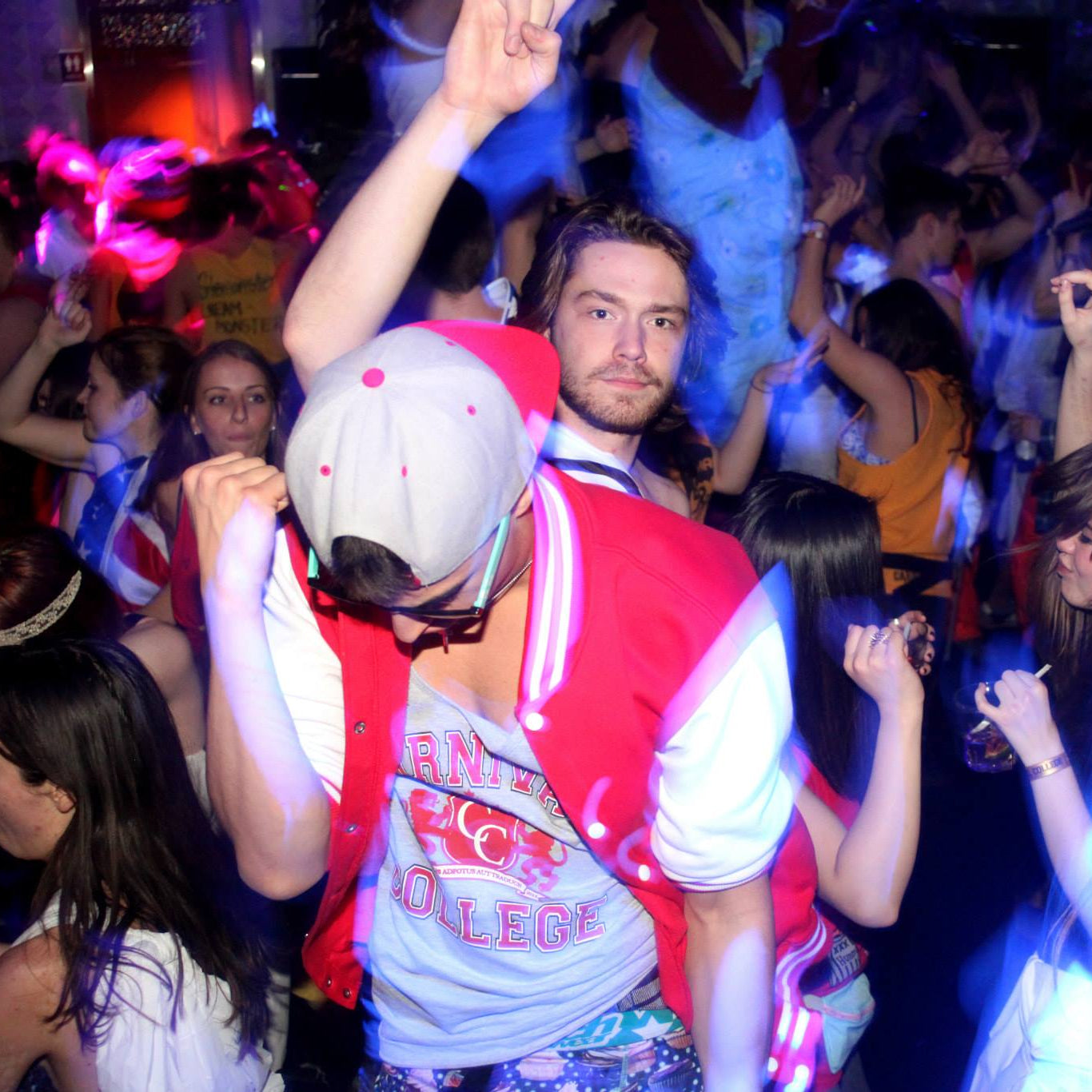 People dancing at a party with colorful lights and a logo in the corner.