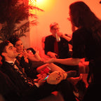 People in a dimly lit room with red lighting, one person holding a plush toy.