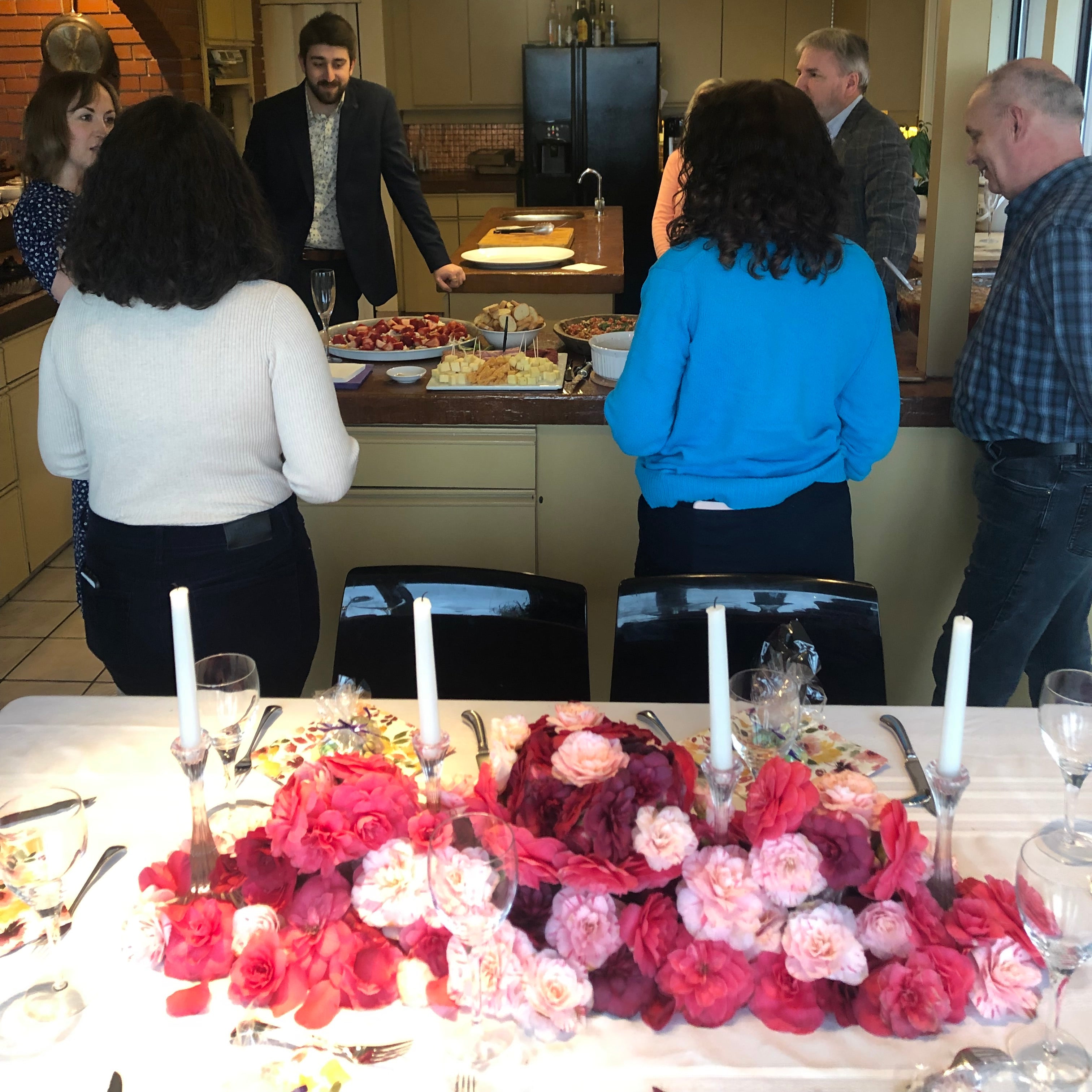 People standing around a table with floral decorations in a restaurant setting.