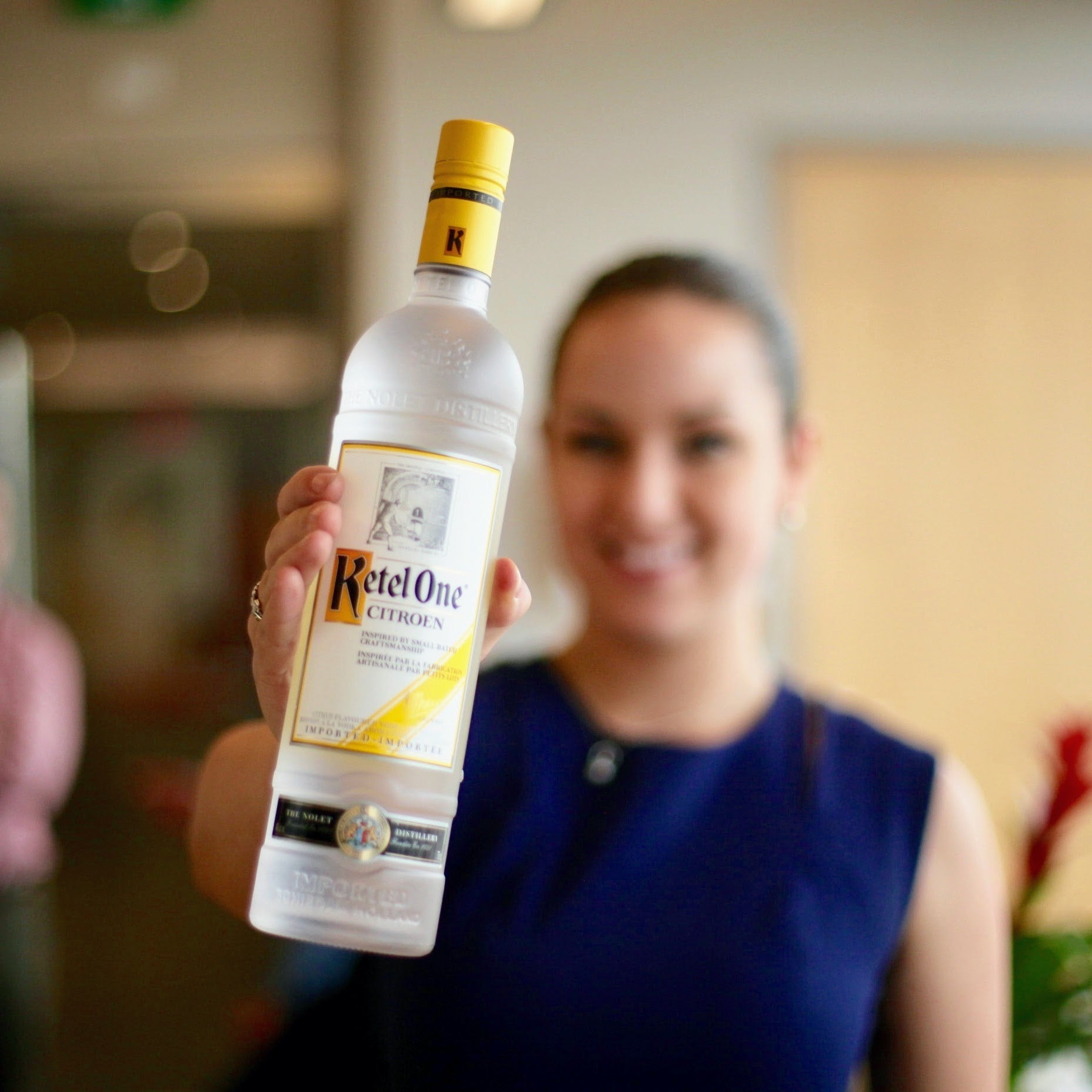 Person holding a bottle of Ketel One vodka in an indoor setting