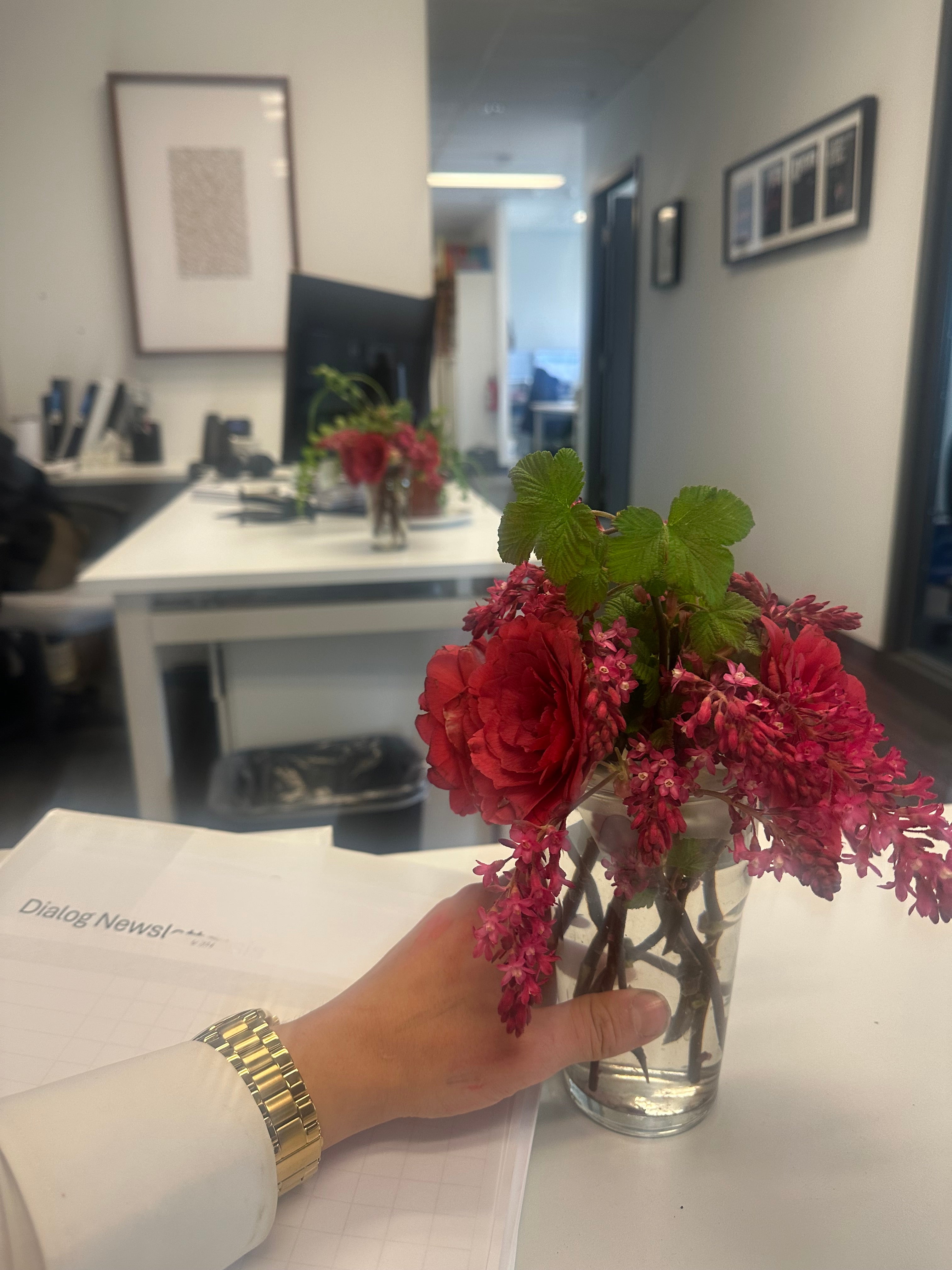Person holding a vase of red flowers in an indoor corporate office setting