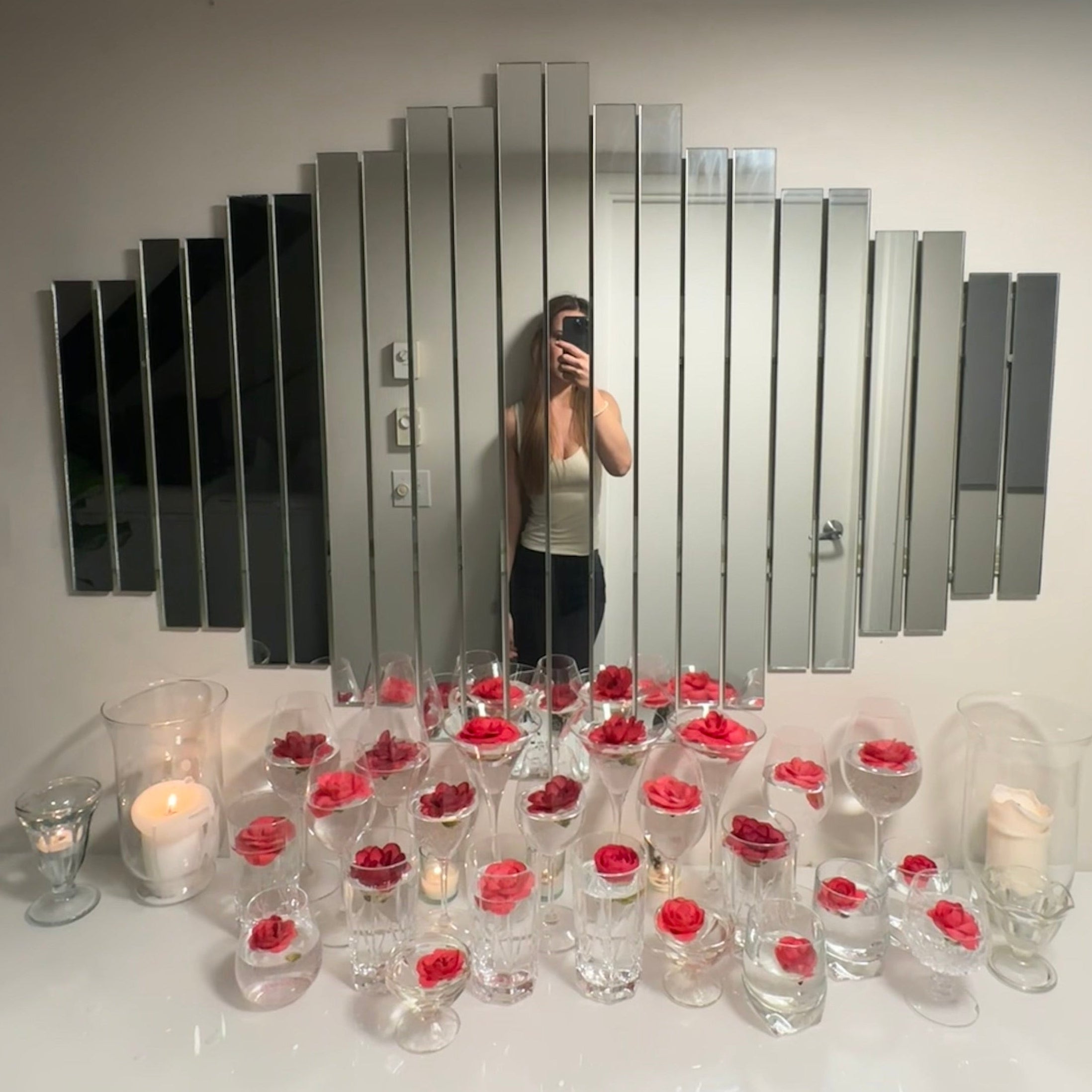 Person taking a mirror selfie with a decorative wall mirror featuring a geometric design.