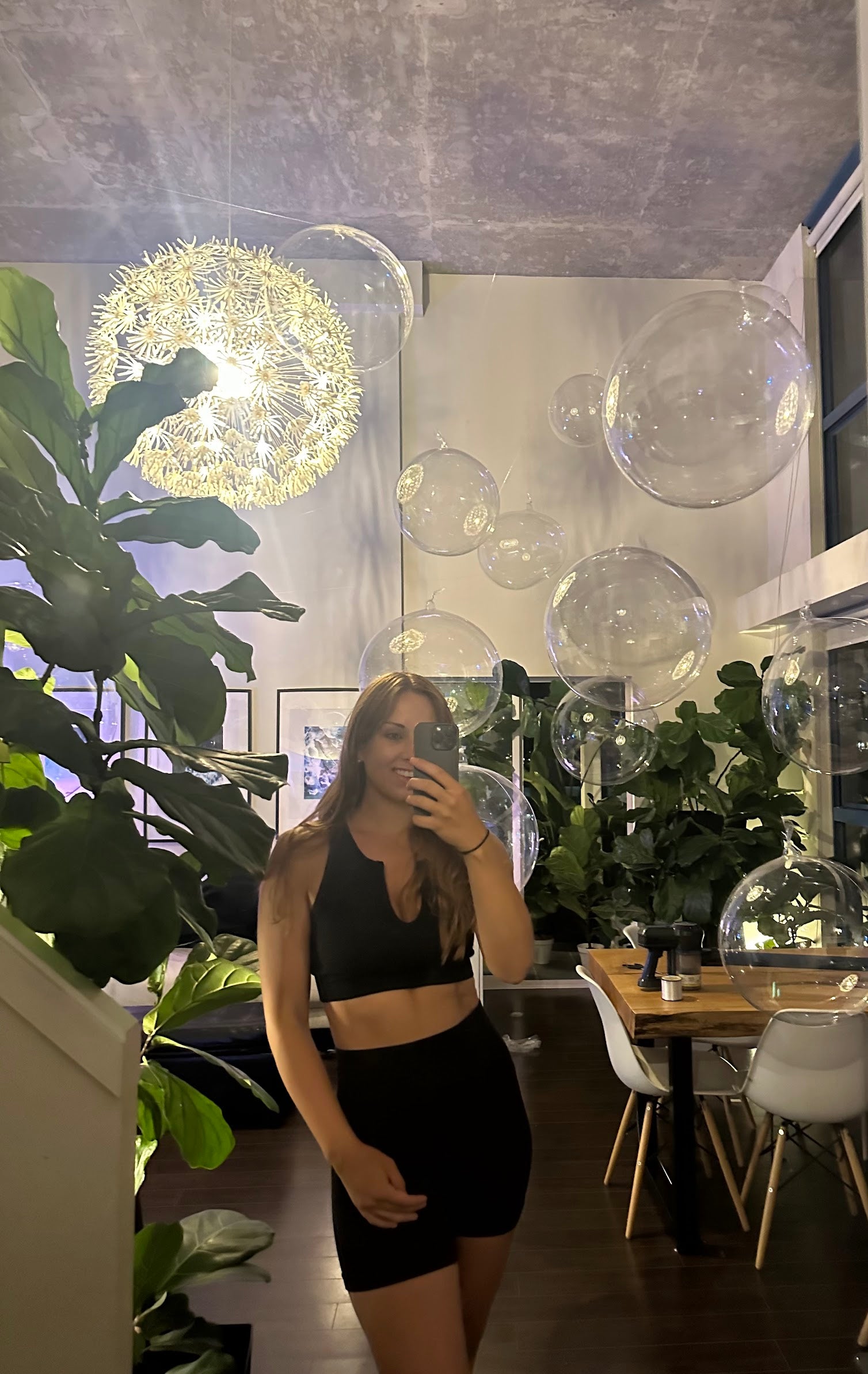 Person taking a mirror selfie in a modern interior setting with plants and decor.