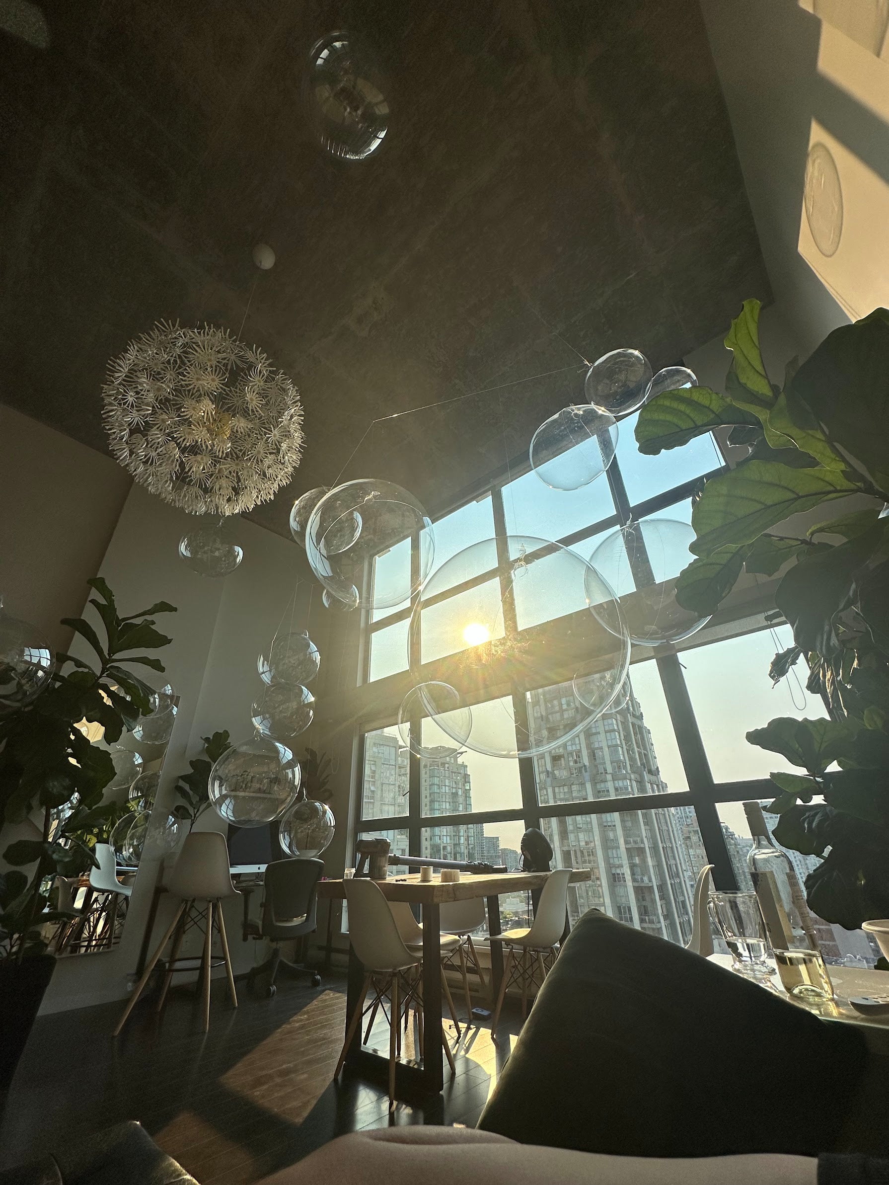 Modern restaurant interior with large windows, chandeliers, and indoor plants.