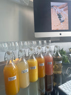 Bottles of different types of juice on a desk with a computer monitor in the background.