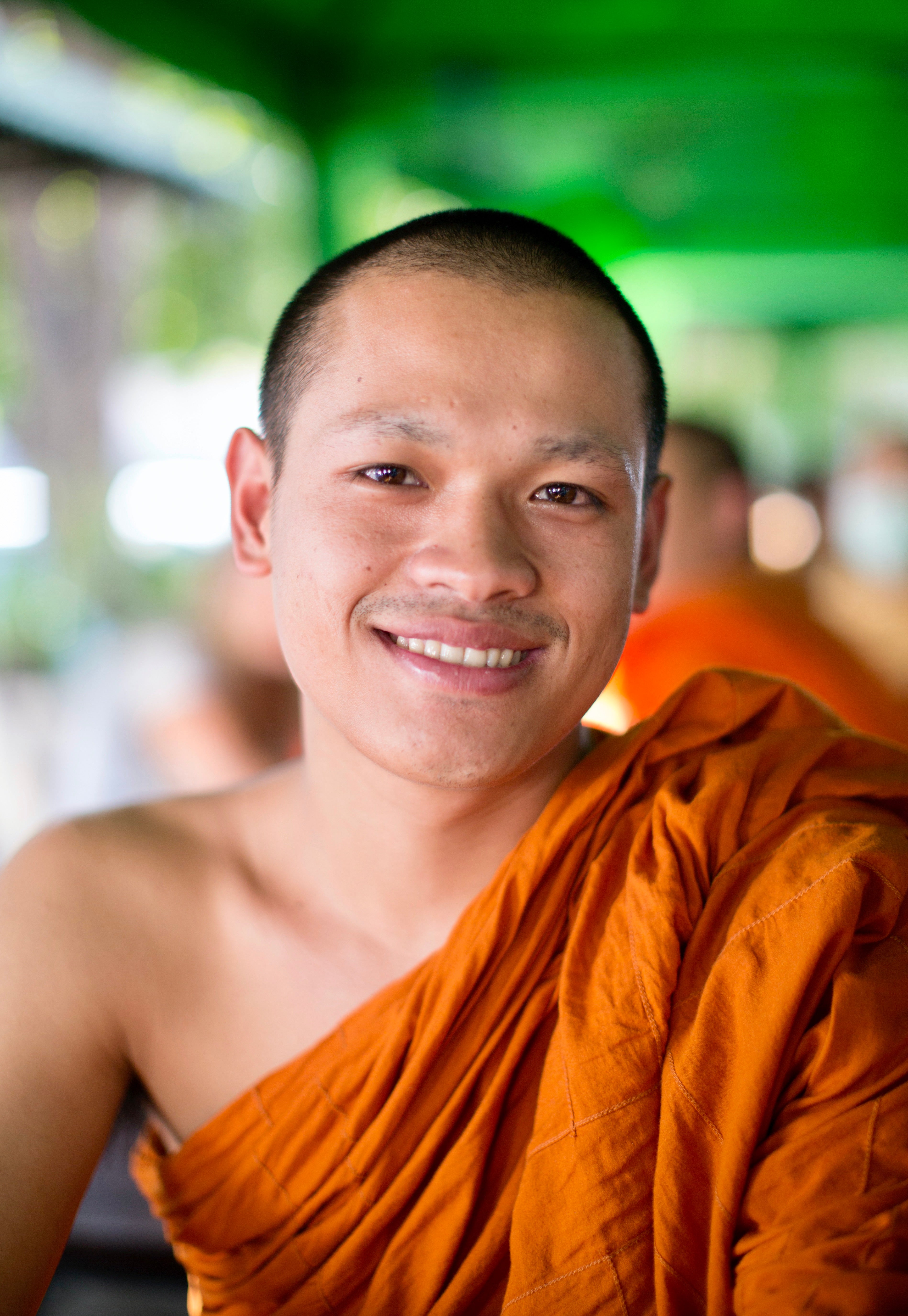 Monk in orange robes smiling outdoors with a blurred background
