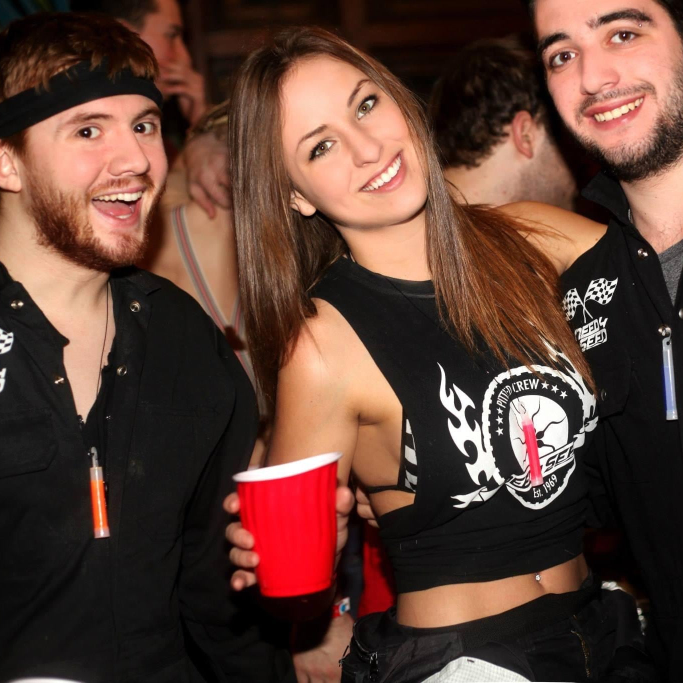 Three friends at a party, two men and a woman, holding red cups.
