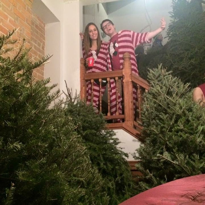 Three people in matching striped outfits standing among Christmas trees indoors.