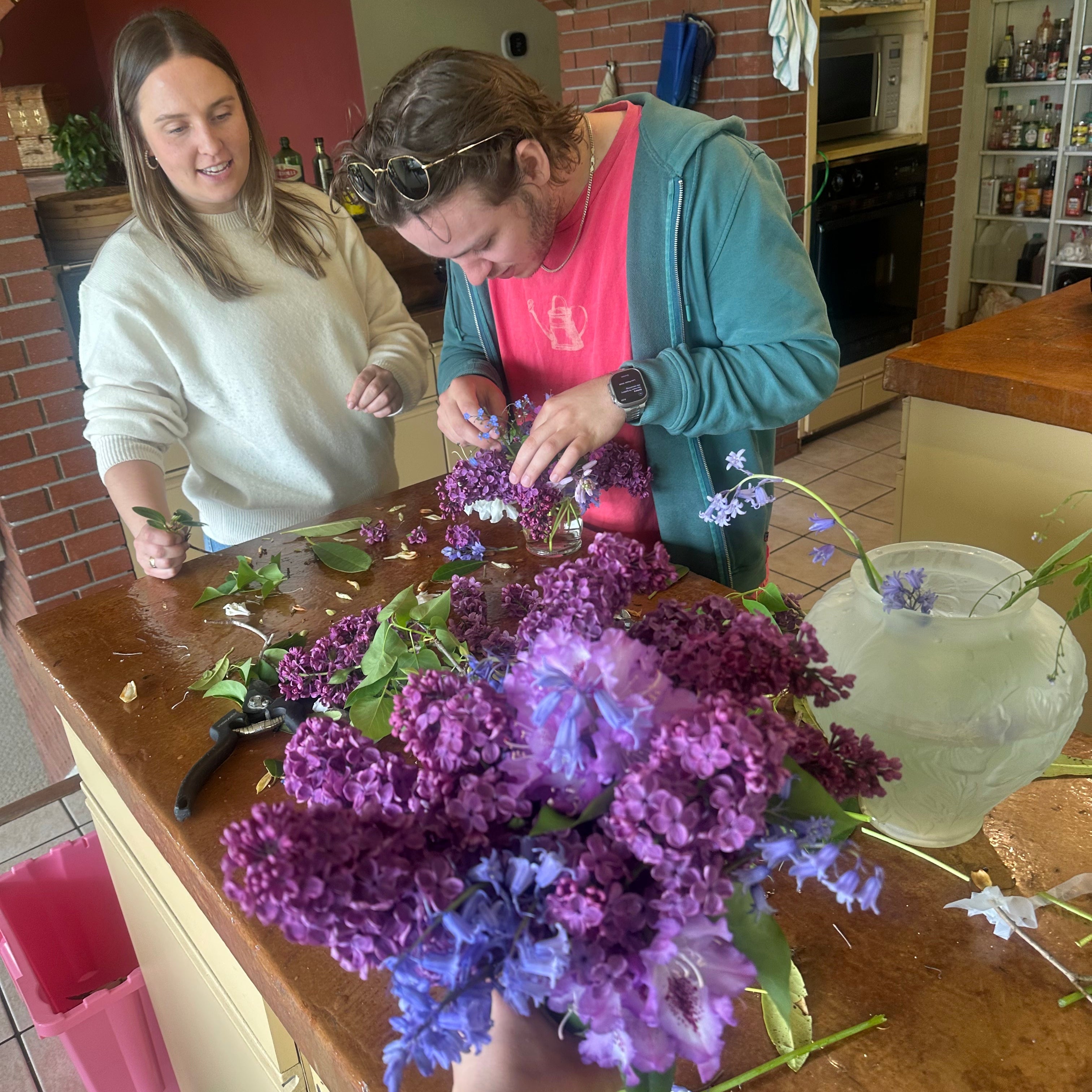 Two people at a table with a large bouquet of purple flowers in a restaurant setting.