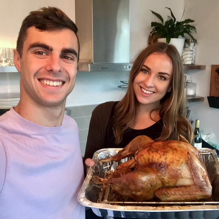 Two people holding a roasted turkey in a kitchen.