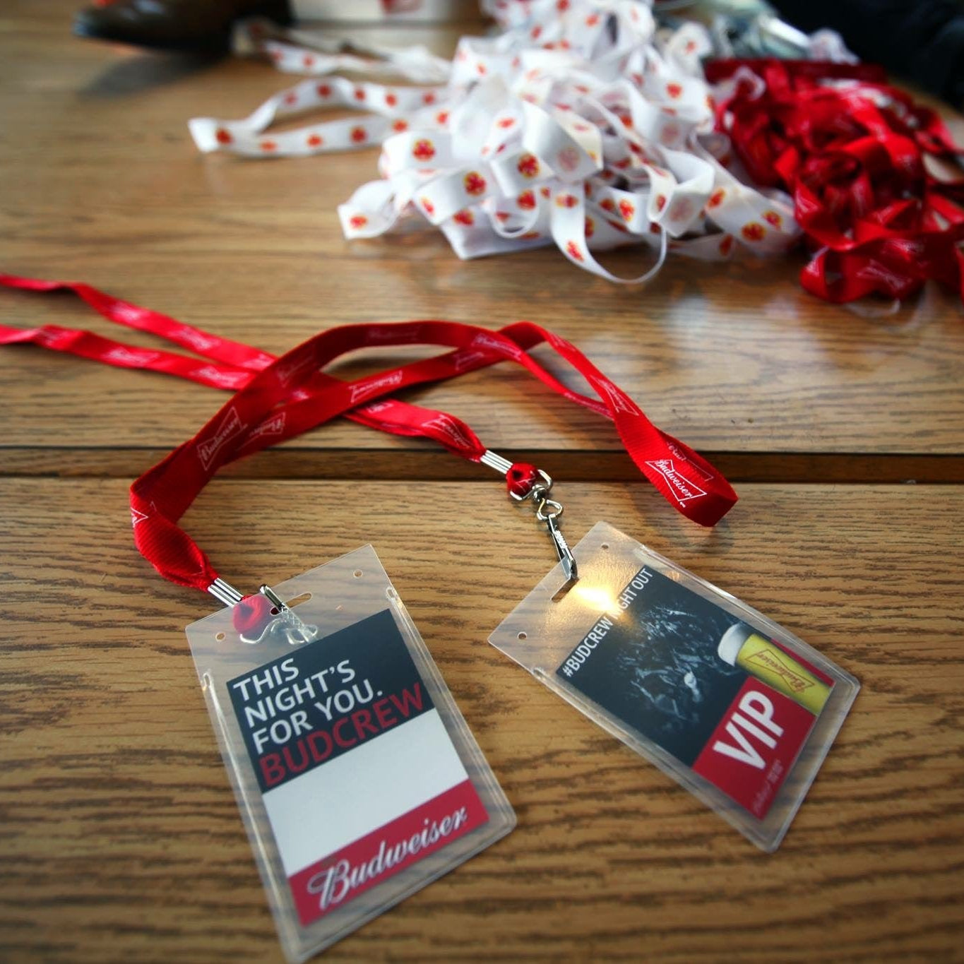 Two plastic badges on a wooden surface with ribbons in the background