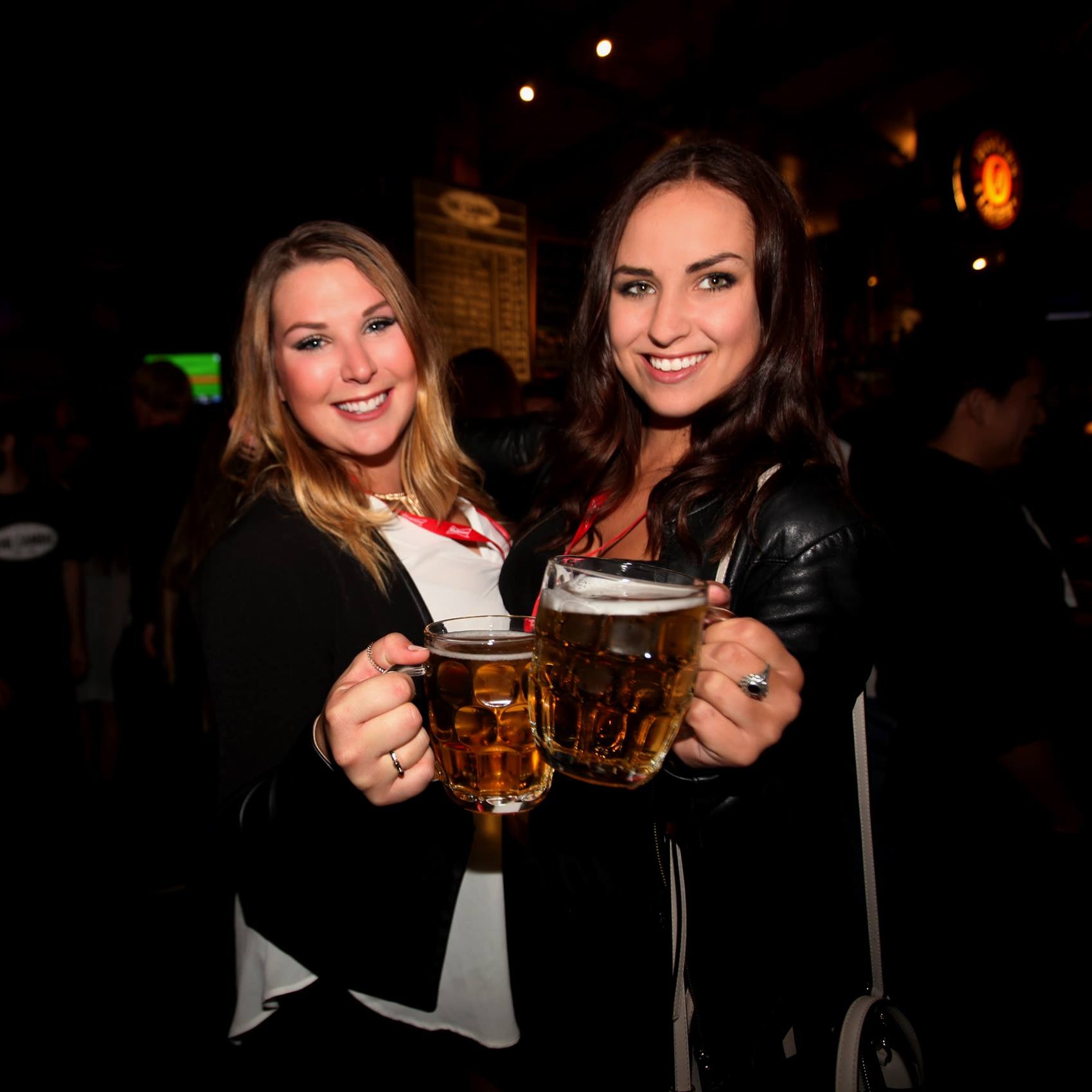 Two women holding beer mugs in a bar setting