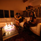 Two women sitting on a couch in a dimly lit room with candles and books.