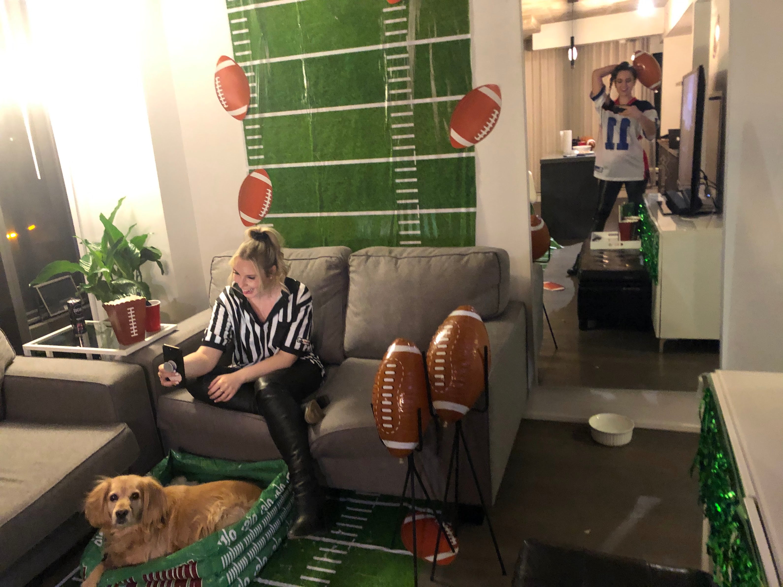 Living room with a person in a referee costume sitting on a couch, a dog in a pet bed, and football decorations.